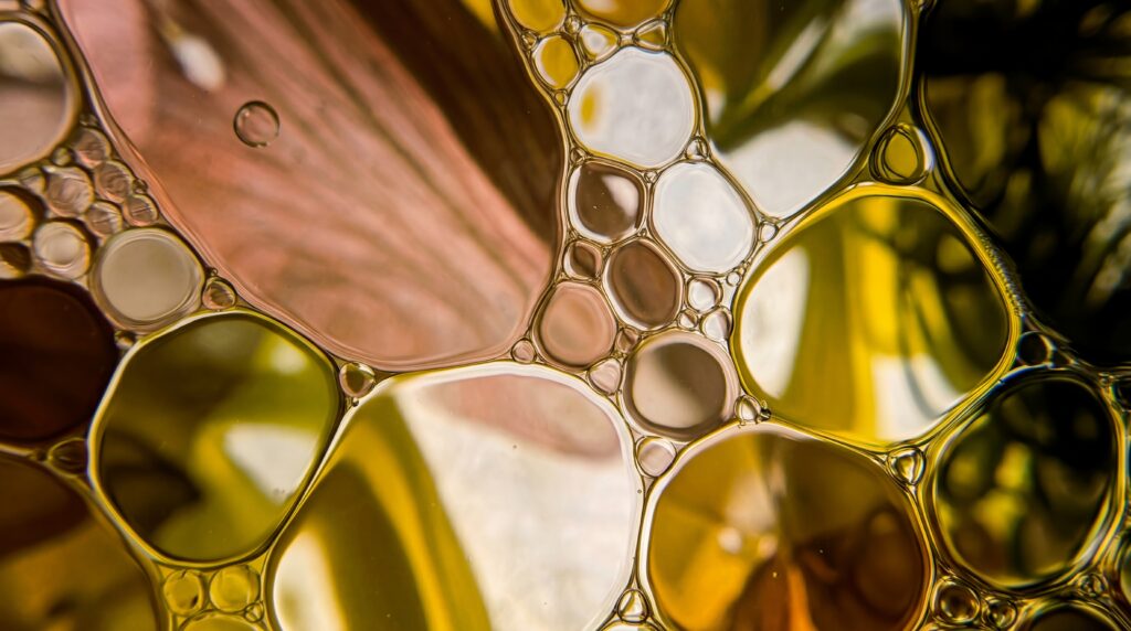 Nahaufnahme von goldgelben Öltröpfchen im Wasser, die ein komplexes, organisches Zellmuster bilden.