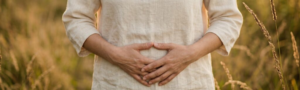 Frau mit Händen auf dem Unterbauch im Freien als Symbol für Unterleibsschmerzen